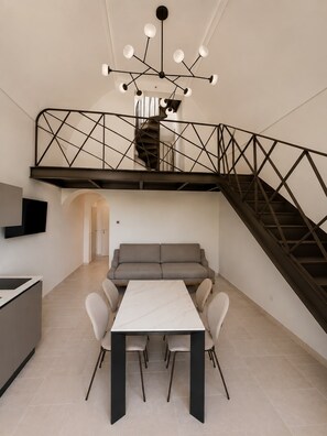 Un interior moderno con comedor, sofá, escalera y televisor montado en la pared.