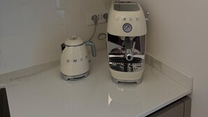 Ett kök med en svart mikrovågsugn placerad ovanför en vit bänkskiva, en vit vattenkokare och en vit kaffemaskin.