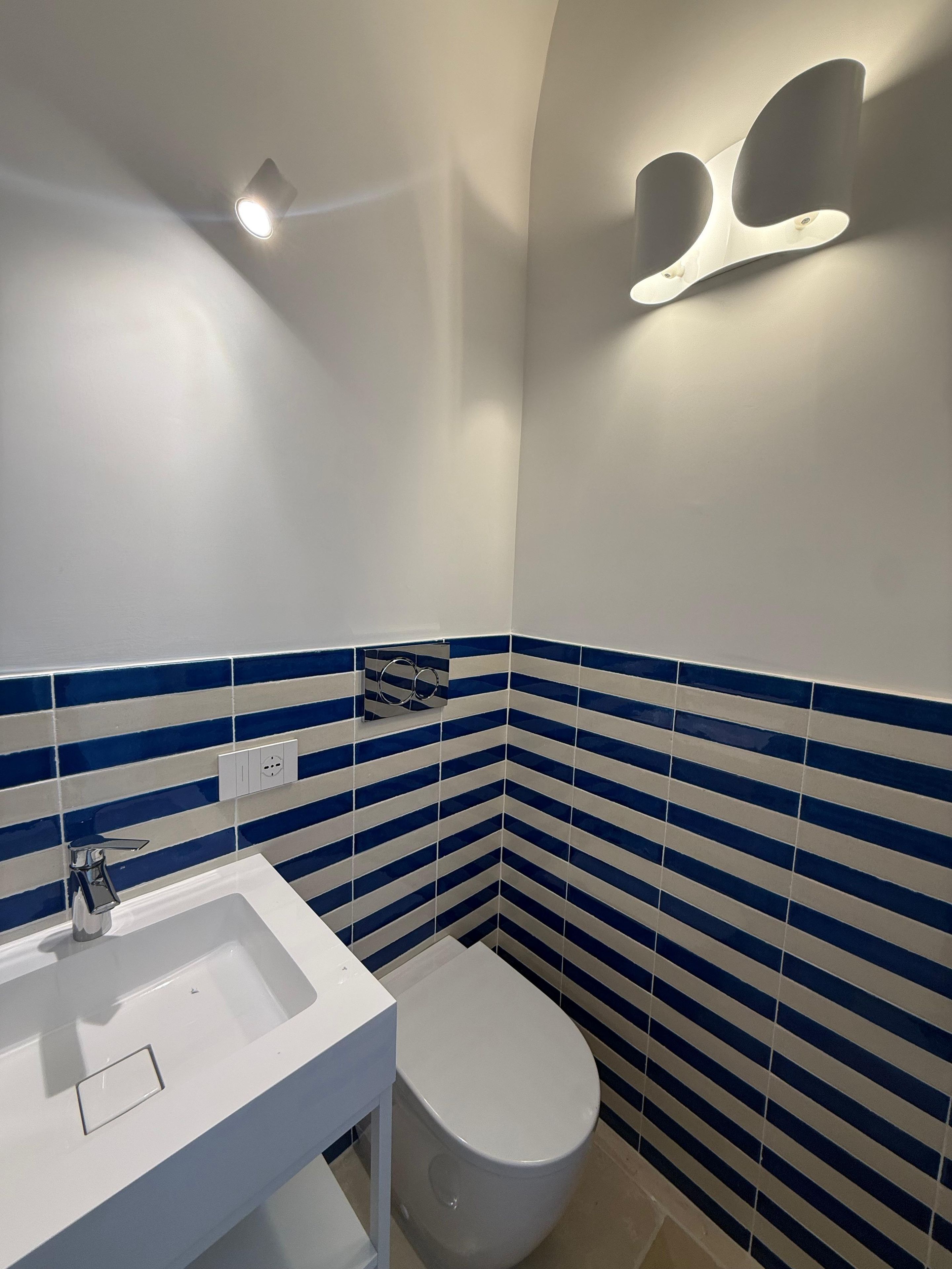 Ein Badezimmer mit einem weißen Waschbecken, einer Toilette und blauen, gestreiften Fliesen an den Wänden.