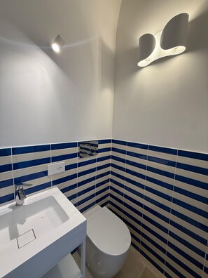 Et badeværelse med en hvid vask, toilet og blåstribede fliser på væggene.