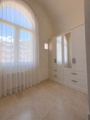 Una habitación con un ventanal grande, un armario con varios cajones y suelo de baldosas.
