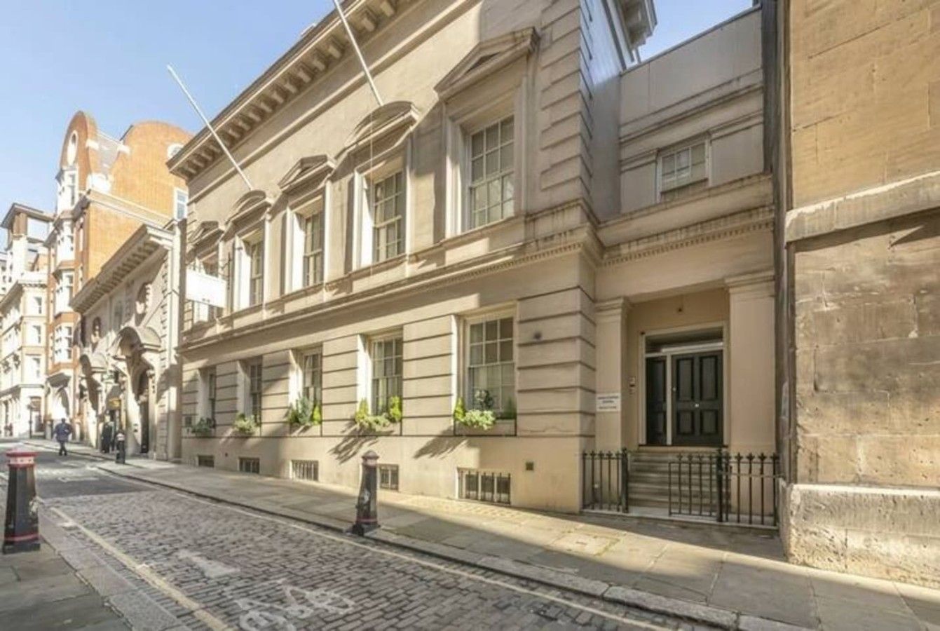 A historic building with a classical facade, a cobblestone street, and a clear sky.