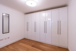 Une pièce avec un plancher en bois, des murs blancs et une grande armoire dotée de poignées argentées.