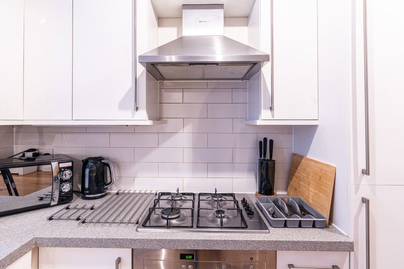 A modern kitchen with white cabinets, a stainless steel range hood, a gas stove, a coffee maker, and a knife block.