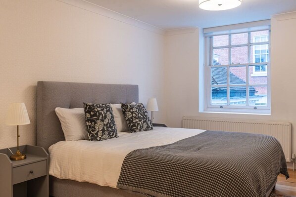 A bedroom with a bed, two bedside lamps, a window, and a radiator. - Historic City of London Gem | 1 Min to Cannon St (Greater London)