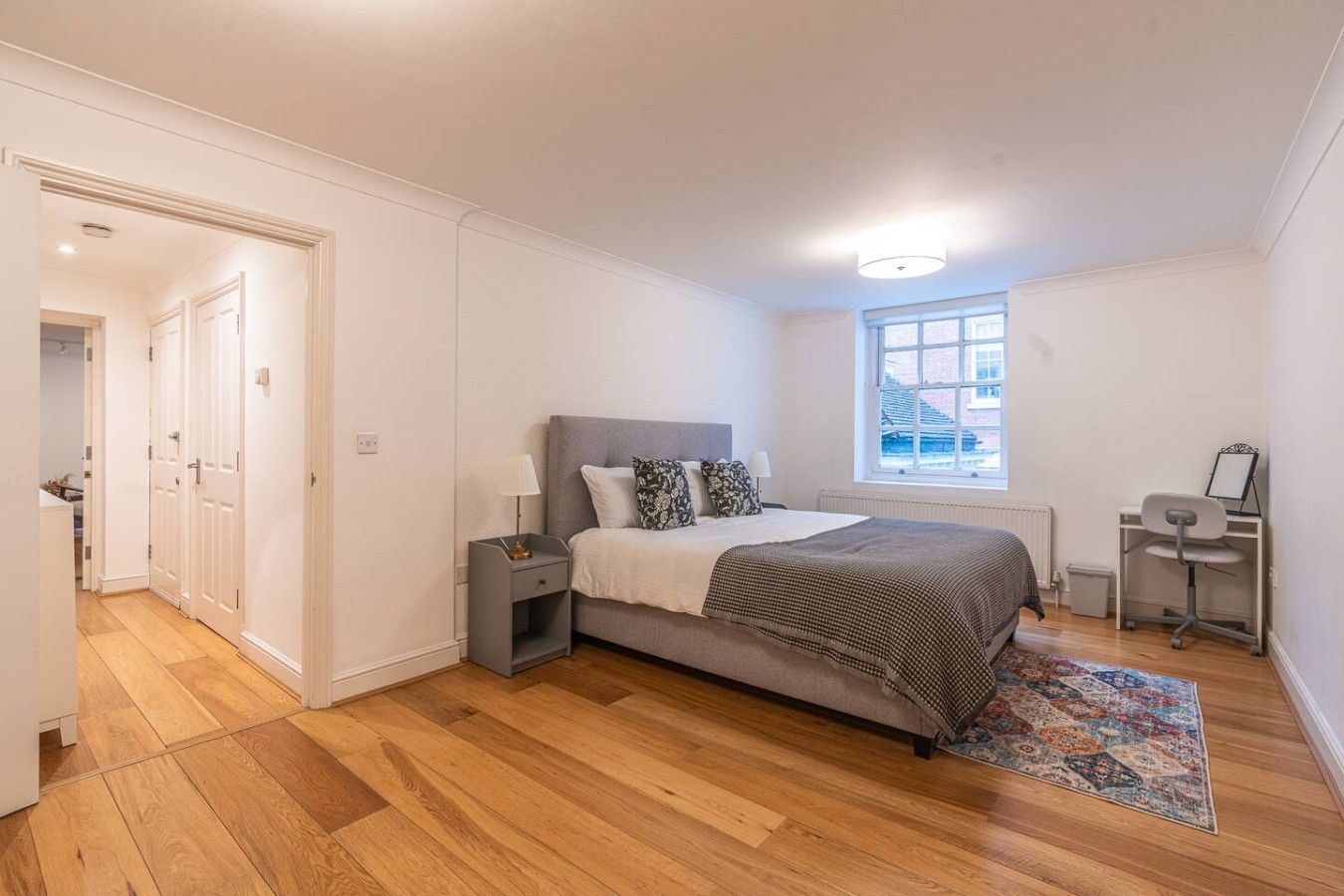 Ein Schlafzimmer mit einem Bett, Nachttischen, einem Fenster und einem Schreibtisch mit Stuhl.