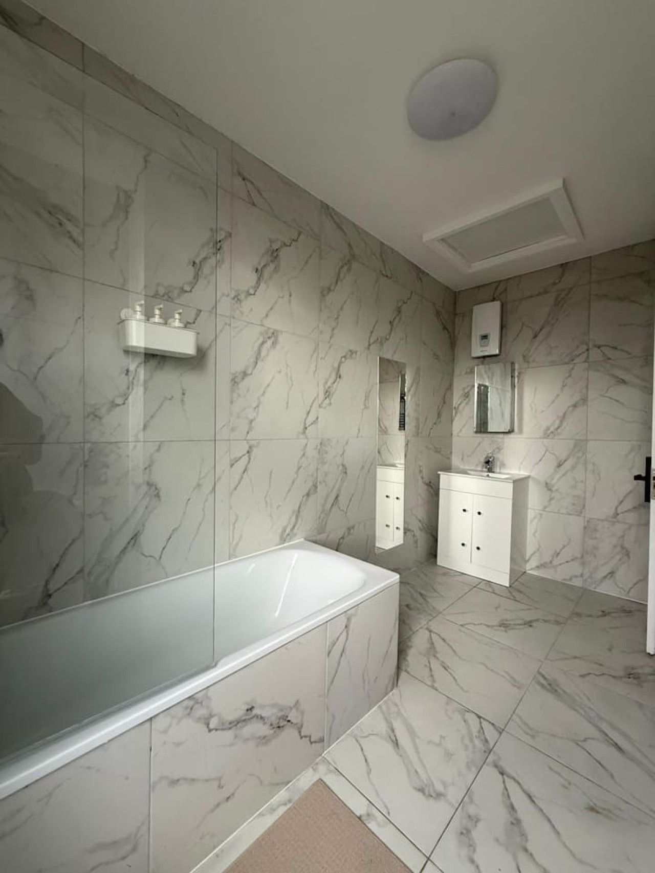 Un bany modern amb sòl de marbre, una banyera independent, un lavabo amb mirall i un escalfador fixat a la paret.
