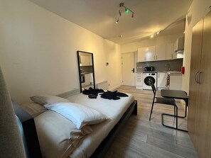 Ein Schlafzimmer mit einem Bett, einem Sessel, einem Tisch, einem Spiegel und einer Küchenzeile im Hintergrund.