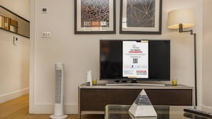 En moderne stue med et fladskærms-tv, et glasbord, en hvid radiator og abstrakte kunstværker i rammer på væggen.