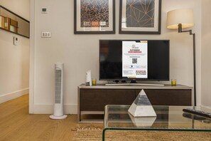Uma sala de estar moderna com televisão de tela plana, mesa de centro de vidro, radiador branco e arte abstrata emoldurada na parede.