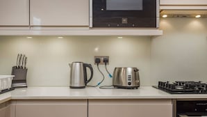 Et moderne køkken med rustfrit stål-hvidevarer, herunder elkedel, brødrister og komfur, med et rent og minimalistisk design.
