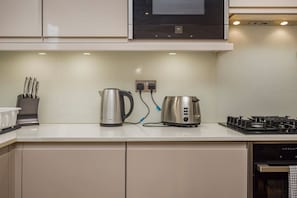 Cozinha moderna com eletrodomésticos de aço inoxidável, incluindo chaleira, torradeira e fogão, com design limpo e minimalista.