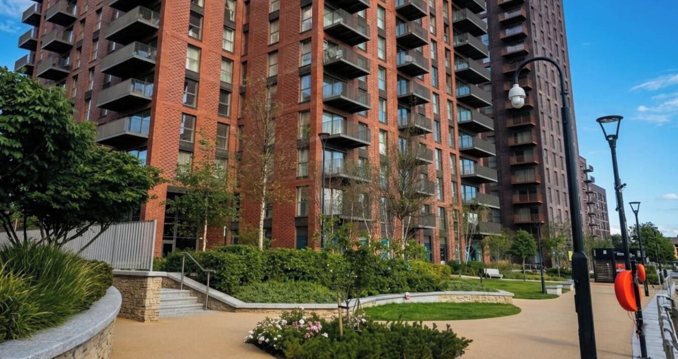 A multi-story residential building with balconies, surrounded by landscaped gardens and a clear sky.