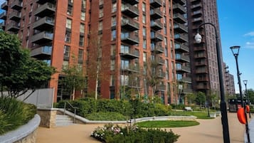 A multi-story residential building with balconies, surrounded by landscaped gardens and a clear sky.