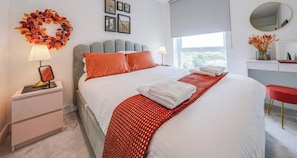 A hotel room with a bed, a nightstand, a desk, a mirror, and a window. - Luxury 2BR | Sleeps 6 | Wembley & Heathrow Direct (London)
