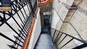 Una escalera metálica con barandilla que lleva a un muro de ladrillo.