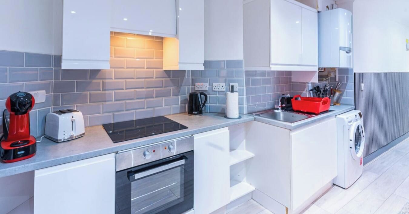 A compact kitchen with a built-in oven, a toaster, a kettle, and a washing machine.