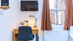 Una habitación con escritorio, silla, televisor y ventana con cortinas.