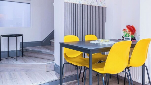 Un comedor con una mesa y cuatro sillas amarillas, una mesita negra y una escultura decorativa de un pez.