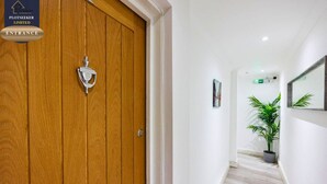 Un pasillo con una puerta de madera, una planta en maceta y un cuadro en la pared.