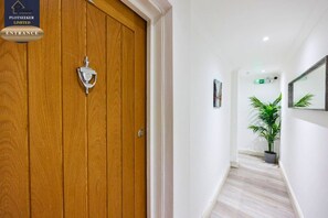 A hallway with a wooden door, a potted plant, and a framed picture on the wall. - Stylish 6BR | 6 En-Suite Showers | Sleeps 16 (Greater London)