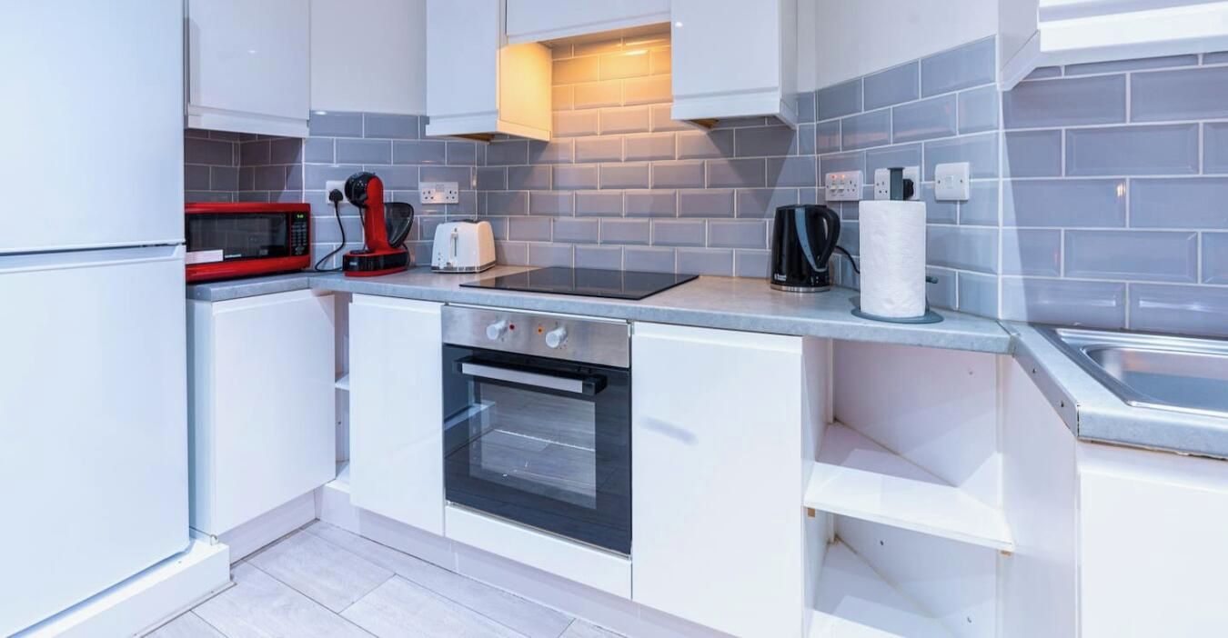 Una cocina moderna con armarios blancos, un microondas rojo, un tostador, una tetera y un lavamanos.