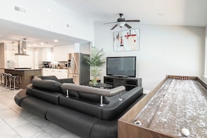A modern living room with a sectional sofa, a flat-screen TV, a ceiling fan, and a pool table. - Luxury SoCo Oasis, Private Pool, Large Covered Patio & Shuffleboard (Austin)
