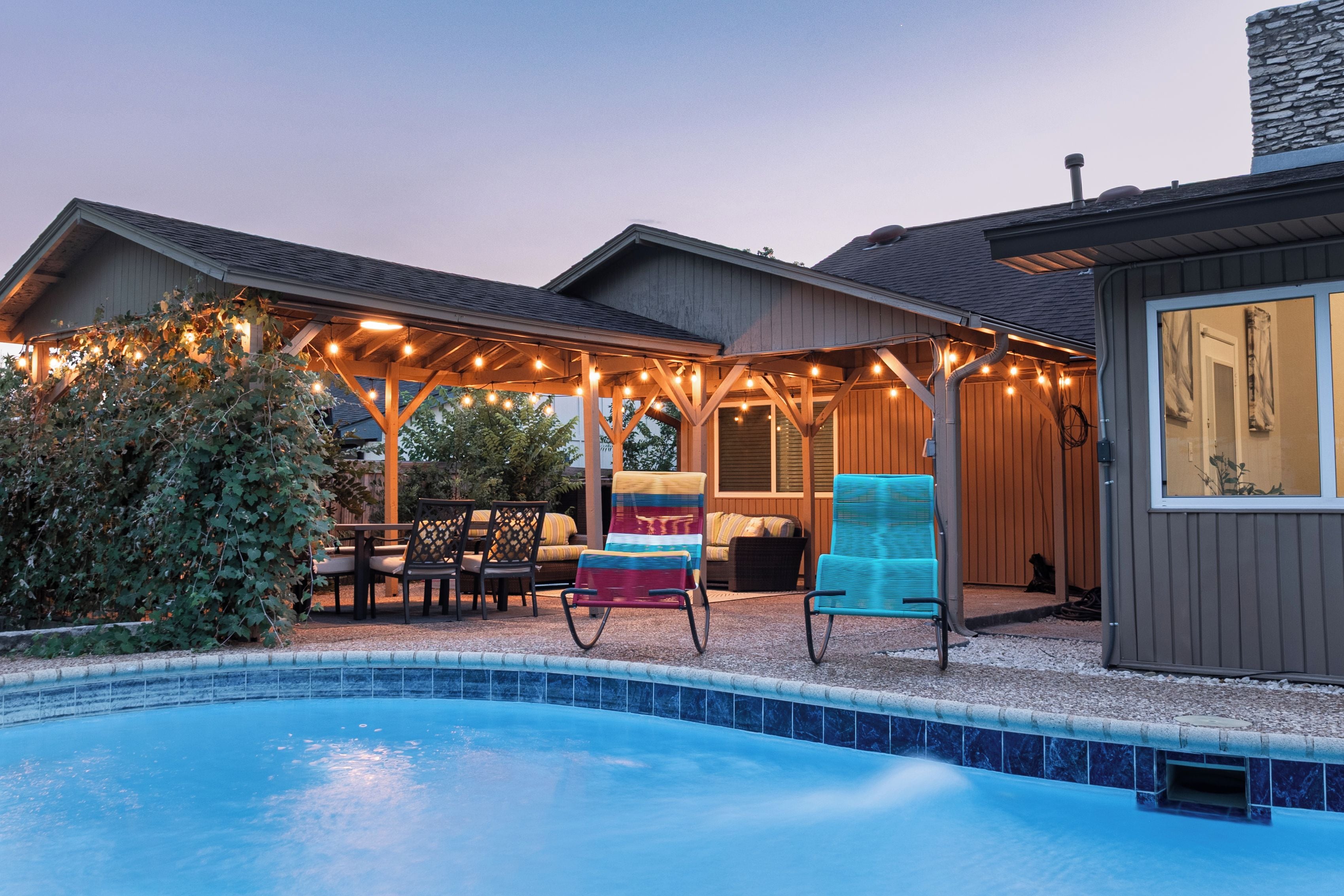 Un espace aménagé au bord de la piscine, avec un patio couvert, du mobilier d’extérieur et des guirlandes lumineuses.