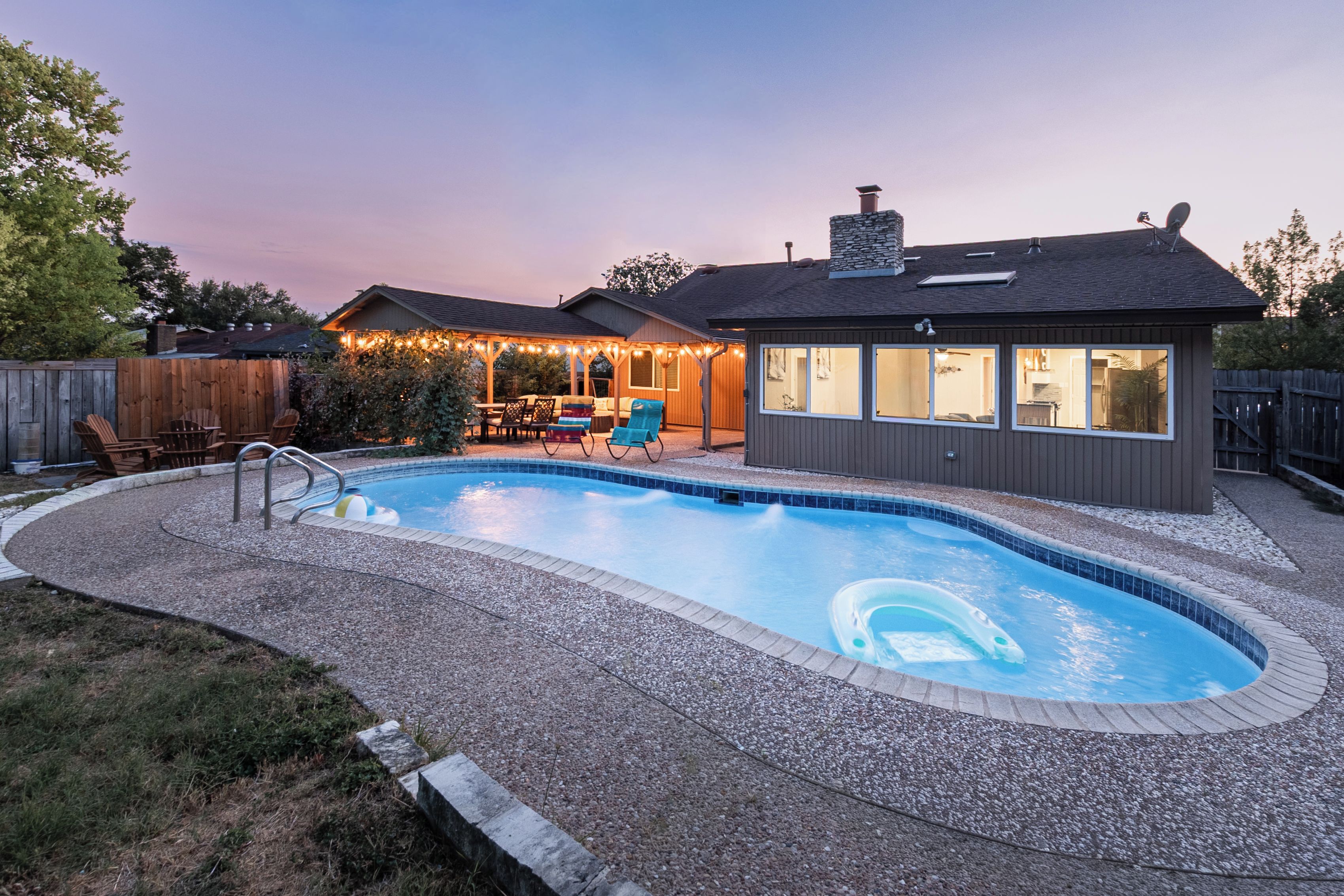 Ein Garten mit Swimmingpool, einer überdachten Terrasse und einem Haus mit großen Fenstern.