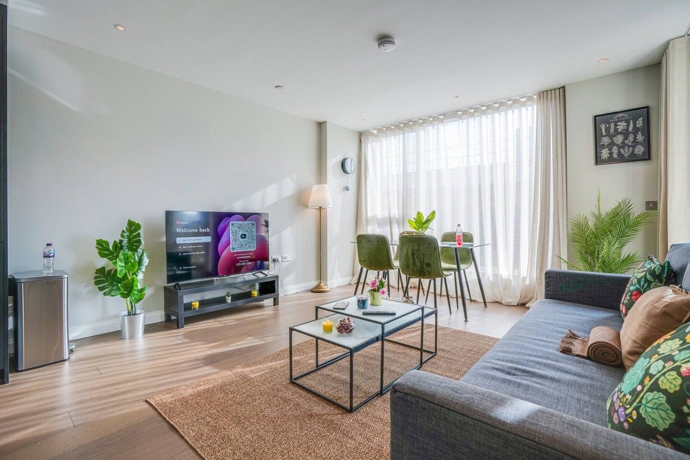 A modern living room with a flat-screen TV, a sofa, a coffee table, and a dining area with chairs.