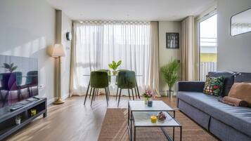 A modern living room with a flat-screen TV, a sofa, a coffee table, and a dining area with chairs and a table.