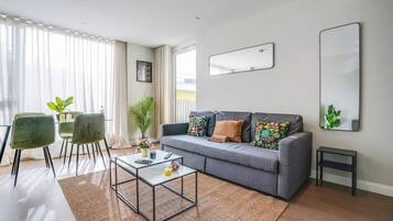 A modern living room with a grey sofa, a glass coffee table, and a small side table.