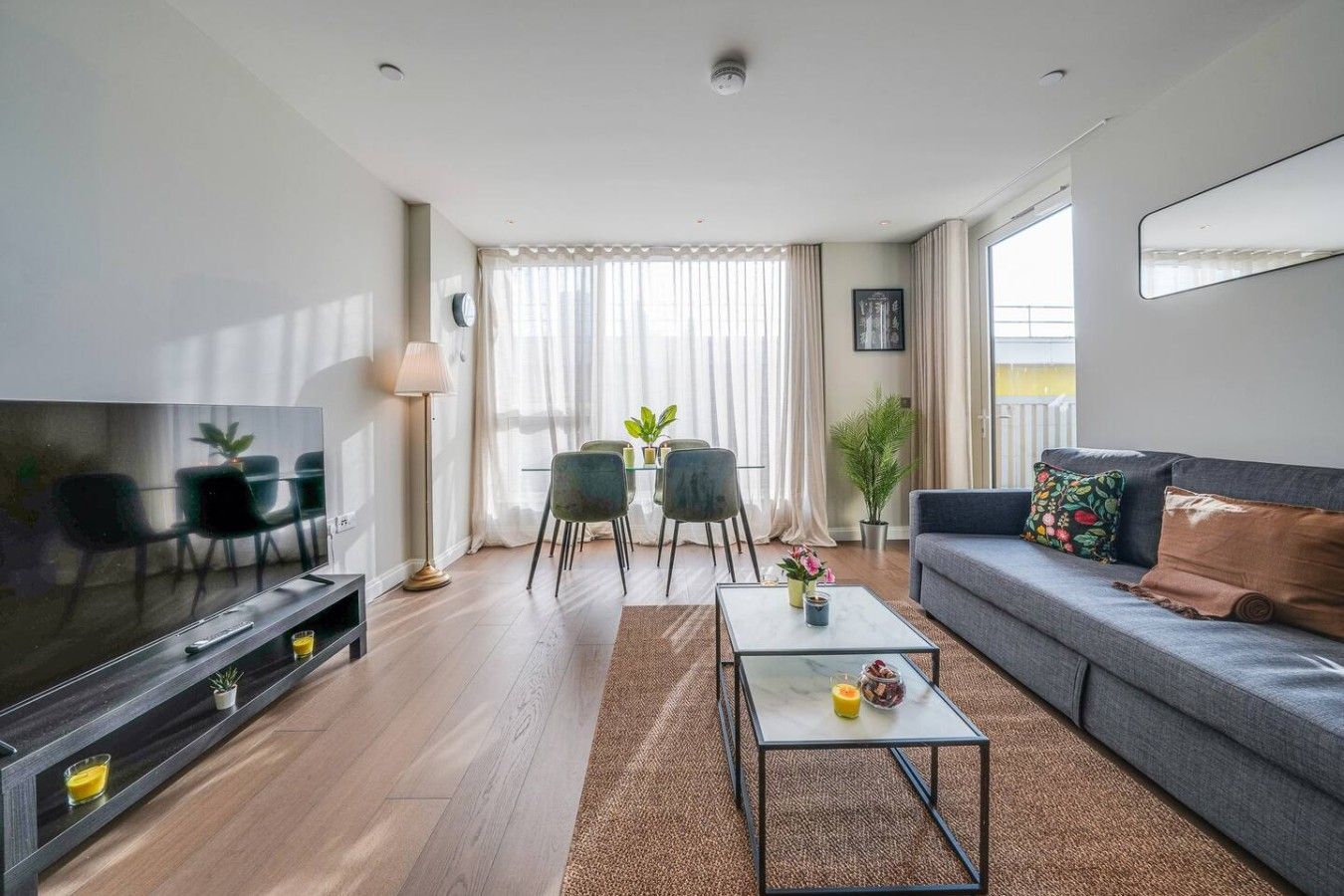 A modern living room with a flat-screen TV, sofa, coffee table, and dining area with chairs and a table.