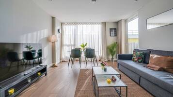 A modern living room with a flat-screen TV, sofa, coffee table, and dining area with chairs and a table.