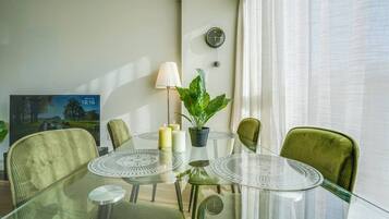 A dining area with a glass table, four chairs, candles, a potted plant, and a wall clock.