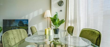 A dining area with a glass table, four chairs, candles, a potted plant, and a wall clock.