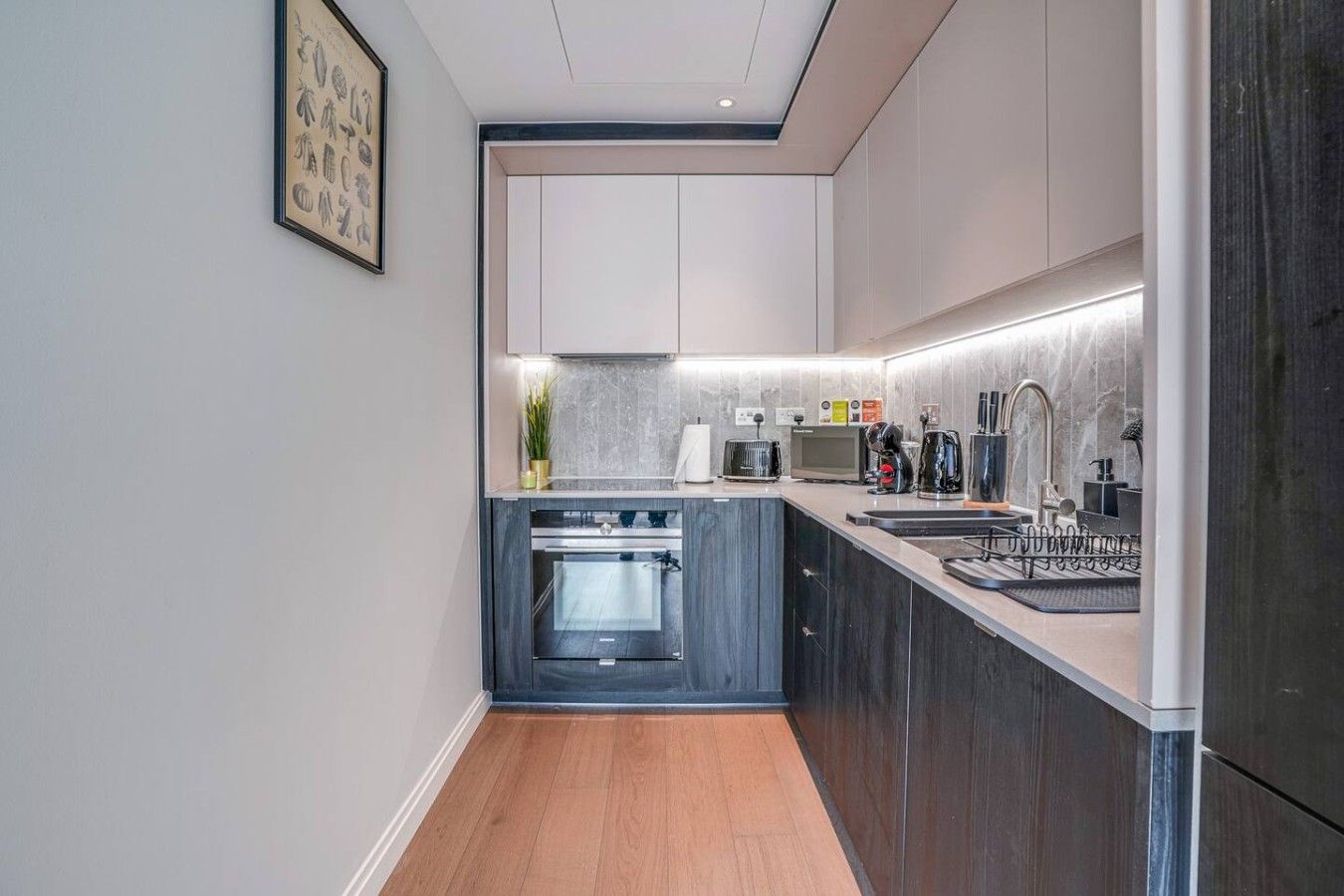 A modern kitchen with a built-in oven, a sink, and a countertop with various appliances.