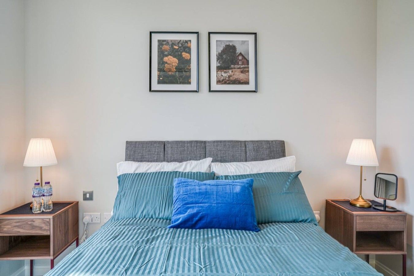 A bedroom with a bed, two nightstands, two lamps, and two framed pictures on the wall.