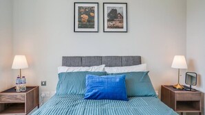 Een slaapkamer met een bed, twee nachtkastjes, twee lampen en twee foto's in een lijst aan de muur.