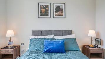 A bedroom with a bed, two nightstands, two lamps, and two framed pictures on the wall.