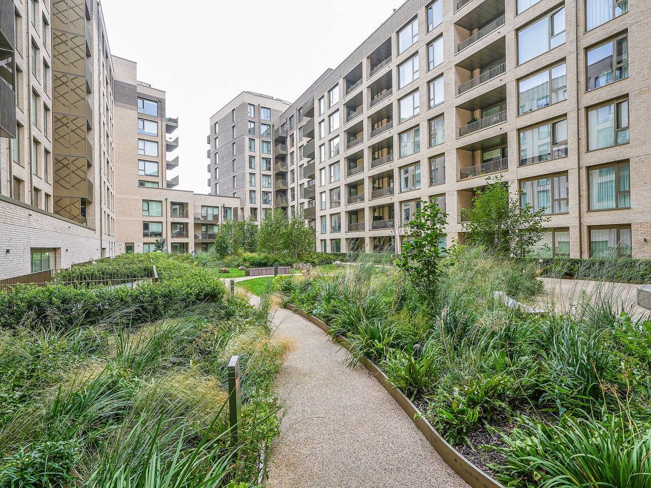 A residential building with multiple balconies and a central pathway surrounded by greenery.