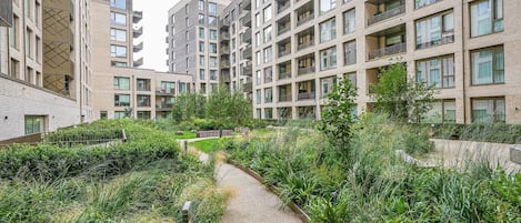 A residential building with multiple balconies and a central pathway surrounded by greenery.