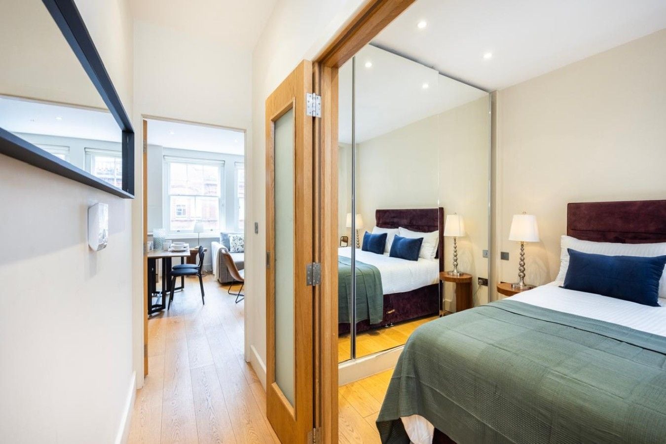 A hotel room with a bed, bedside table, and a mirror reflecting the room.