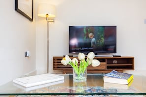 Ein Glastisch mit einer Tulpenvase, einem Buch und einem Fernseher im Hintergrund.
