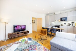 Ein modernes Wohnzimmer mit Fernseher, einer Couch, einem Couchtisch mit einem Buch und einem Essbereich mit Stühlen und einem Tisch.
