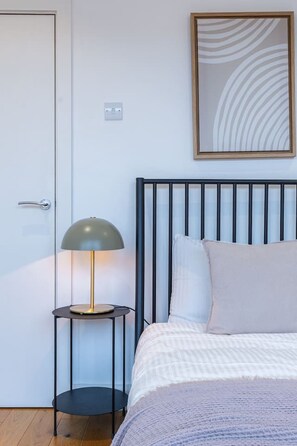A bedroom with a bed, a bedside lamp, a door, and a wall-mounted artwork.