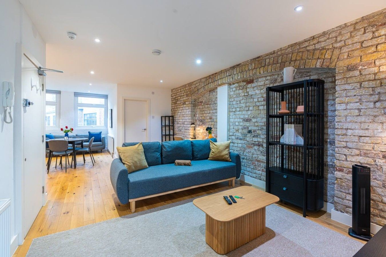 A modern living room with a blue sofa, a wooden coffee table, and a brick wall.