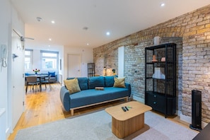 A modern living room with a blue sofa, a wooden coffee table, and a brick wall.