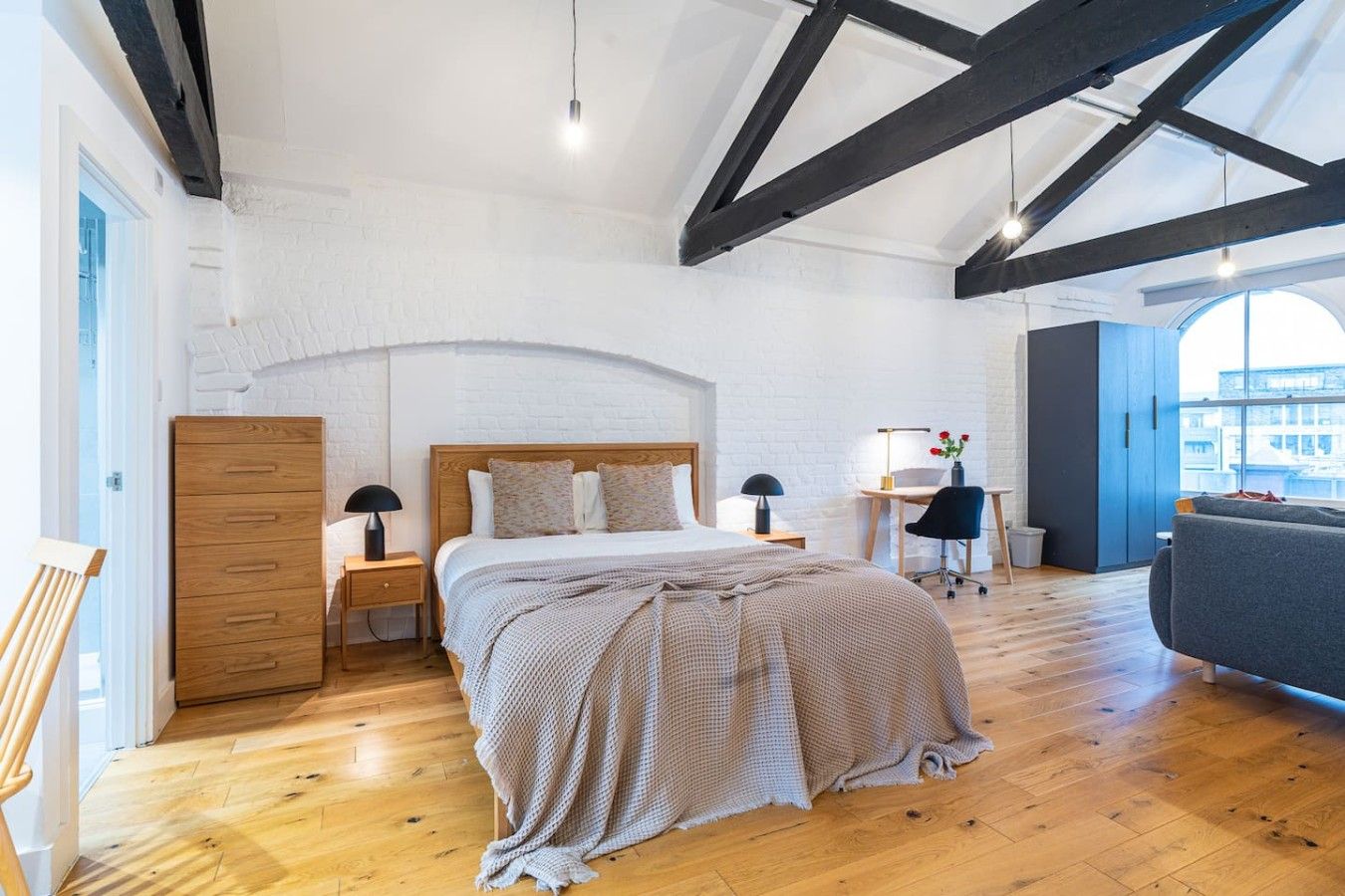 A bedroom with a wooden bed, a desk, a chair, and a large window.