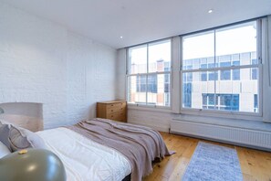 A bedroom with a large window, a bed, a dresser, and a radiator. - Farringdon Entire Building | 4BR | Sleeps 18 (Greater London)